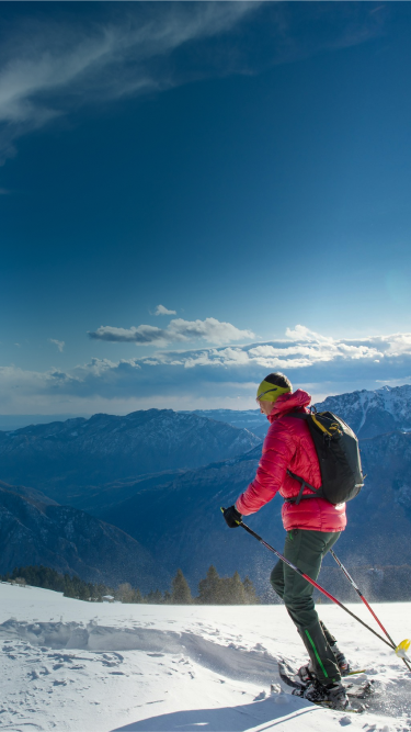 Person in red jacket skiing on snowy mountain with scenic blue sky and distant mountain range in background.