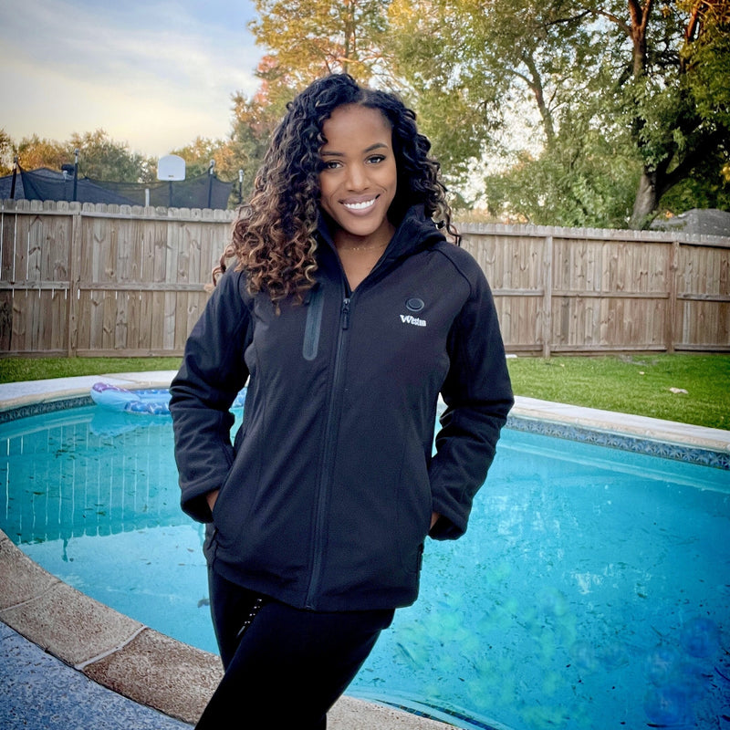 Woman in black jacket smiling by a backyard pool with trees and fence in the background.