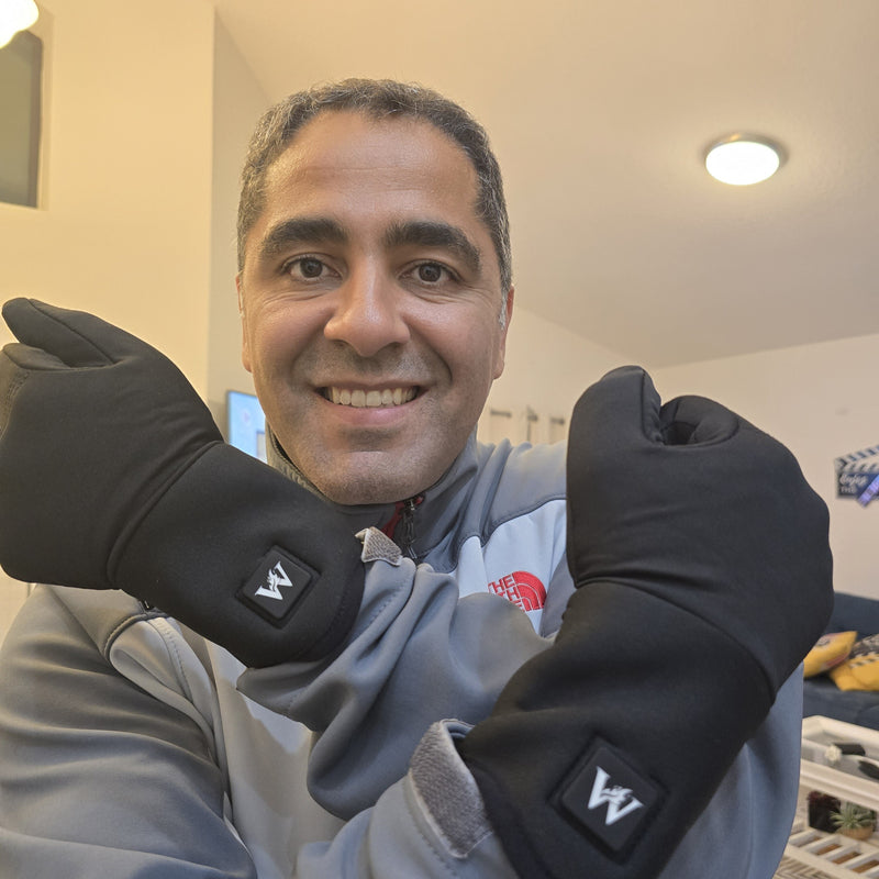 Person smiling and wearing black winter gloves, crossing arms indoors.