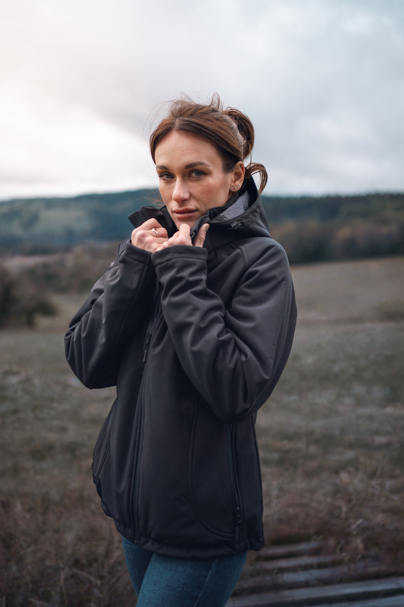 Woman in a black jacket standing outdoors in a rustic landscape, overcast skies