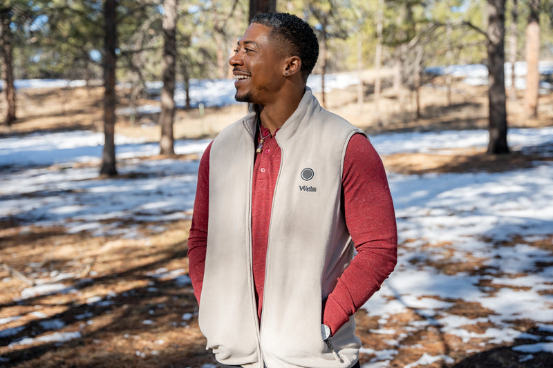 Man wearing a red shirt and beige vest outdoors in a snowy forest setting, smiling and looking to the side.