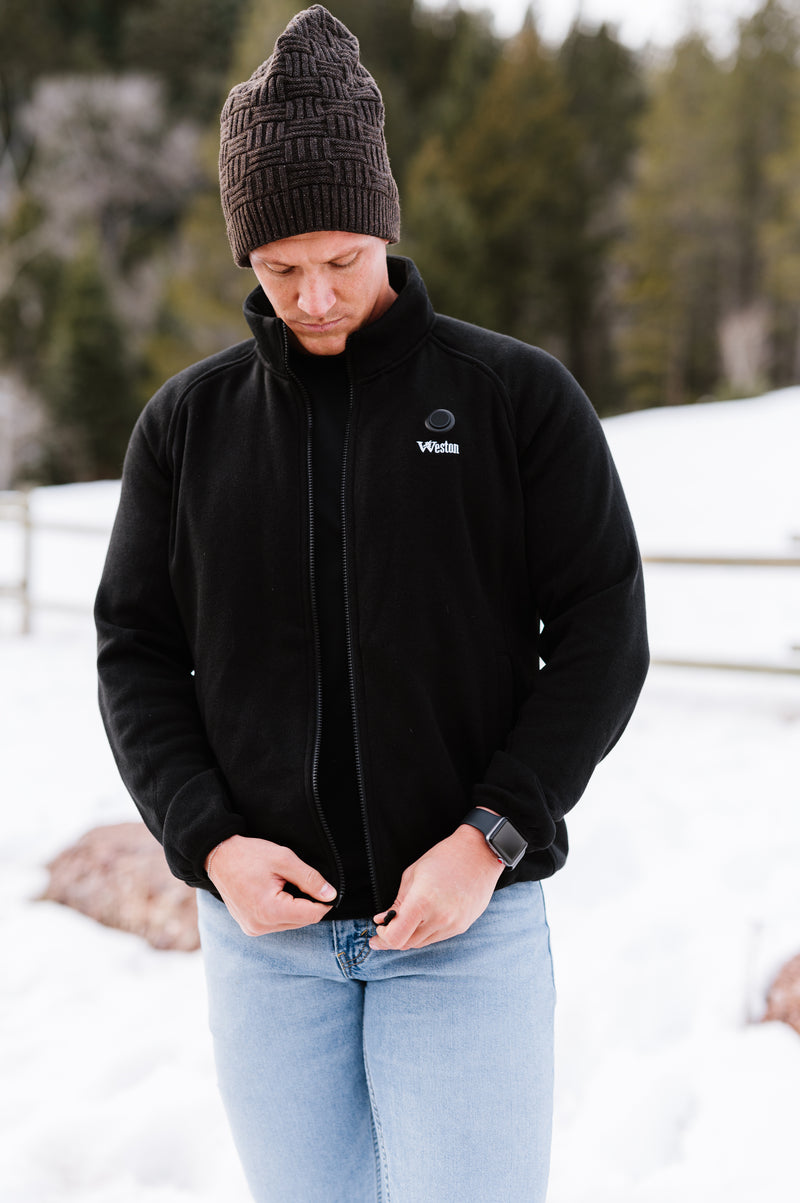 Person wearing a black jacket and brown beanie outdoors in a snowy landscape.